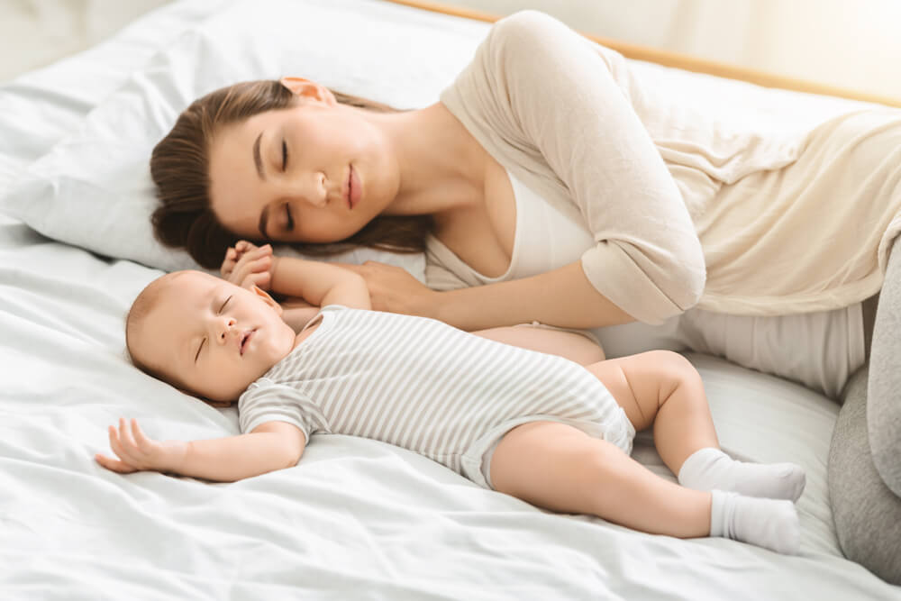 A woman sleeping in bed with her baby.
