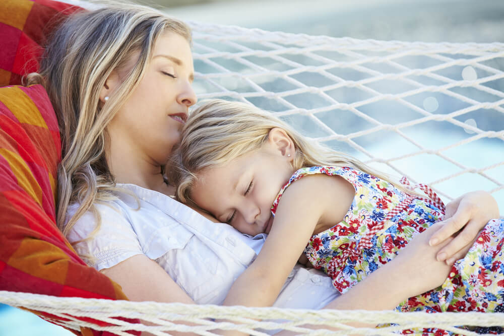 A mother and daughter sleeping together in a hammock.