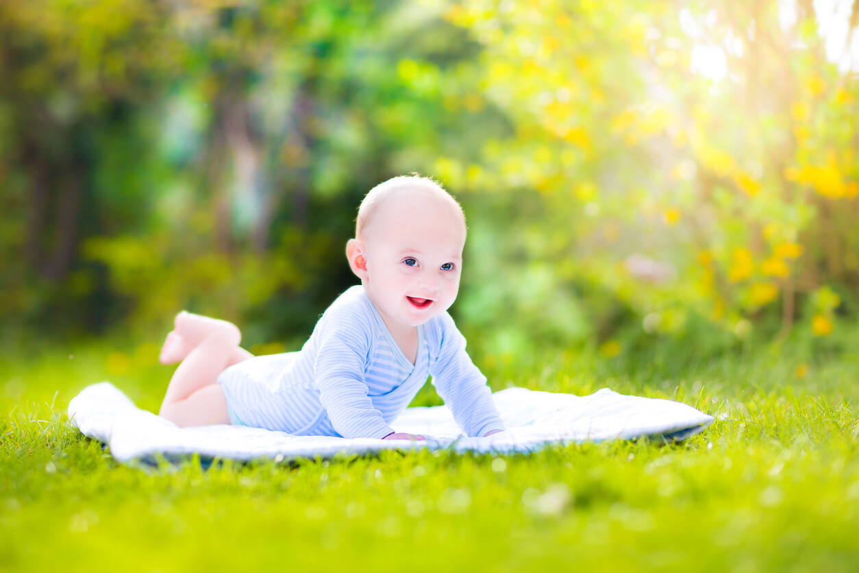 En baby som ligger på et teppe på gresset.