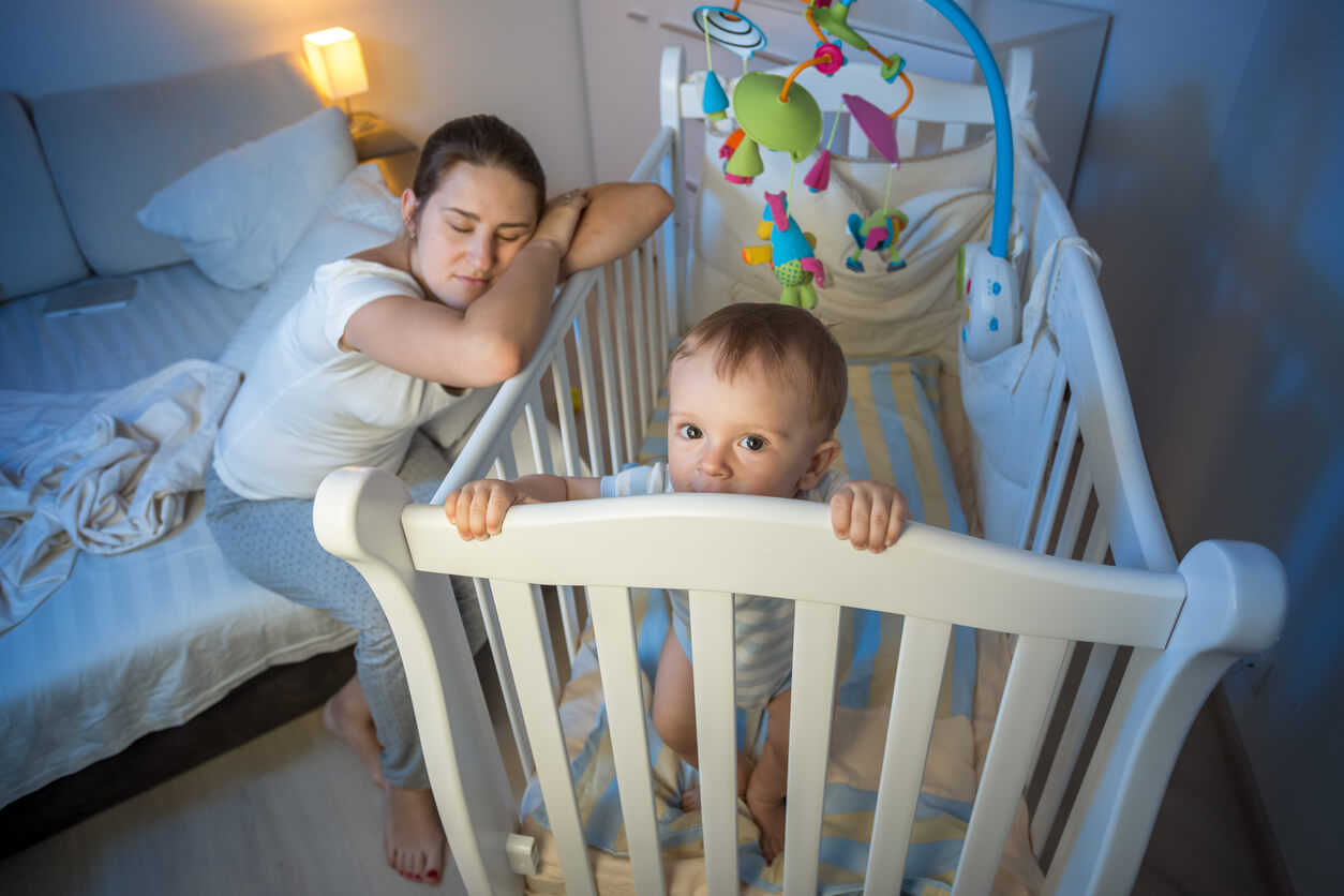 Une mère épuisée qui dort sur le lit de son bébé qui ne dort pas.