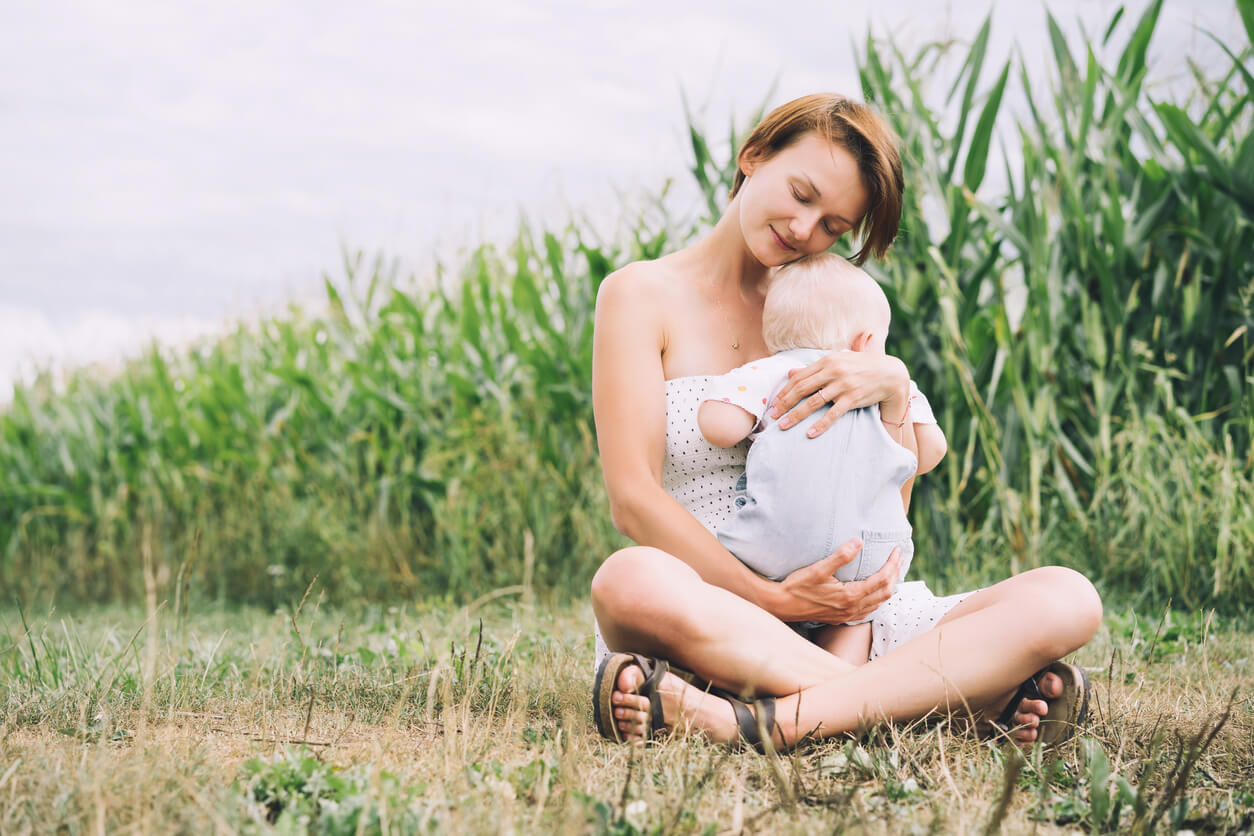 A mother sitting in a field holding her baby.