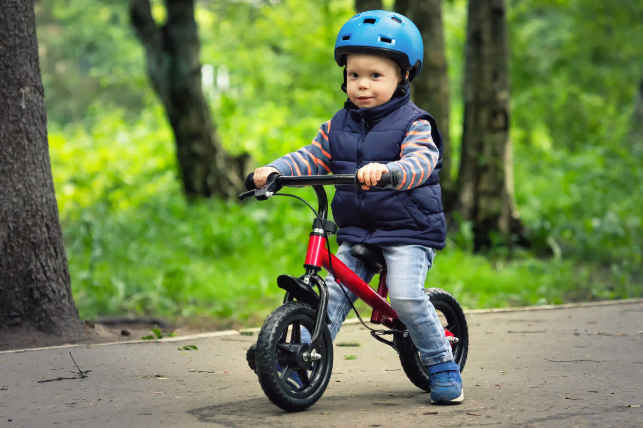 A toddler riding on a balance bike with a helmet.