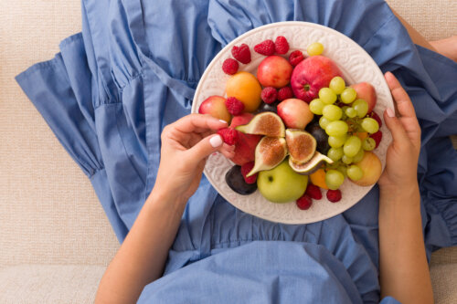 manos de nina joven con plato de frutas sobre la falda