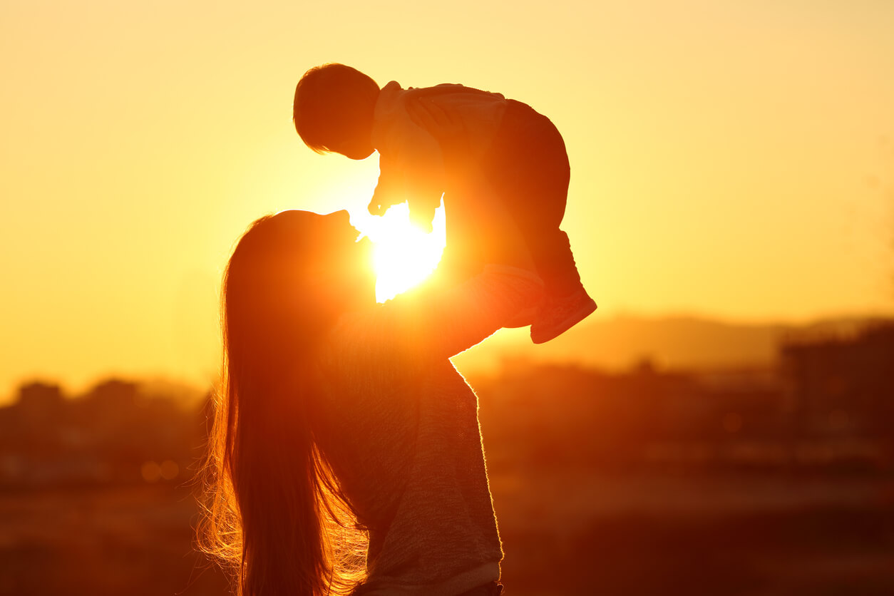 A woman holding her baby up in the air with the sunset in the background.