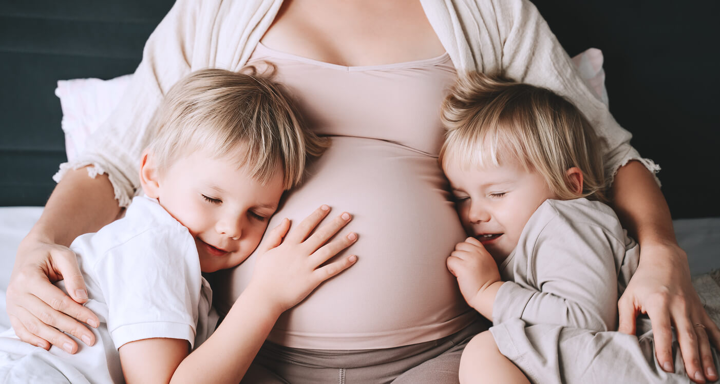 En gravid kvinne som klemmer de små barna sine mot magen.