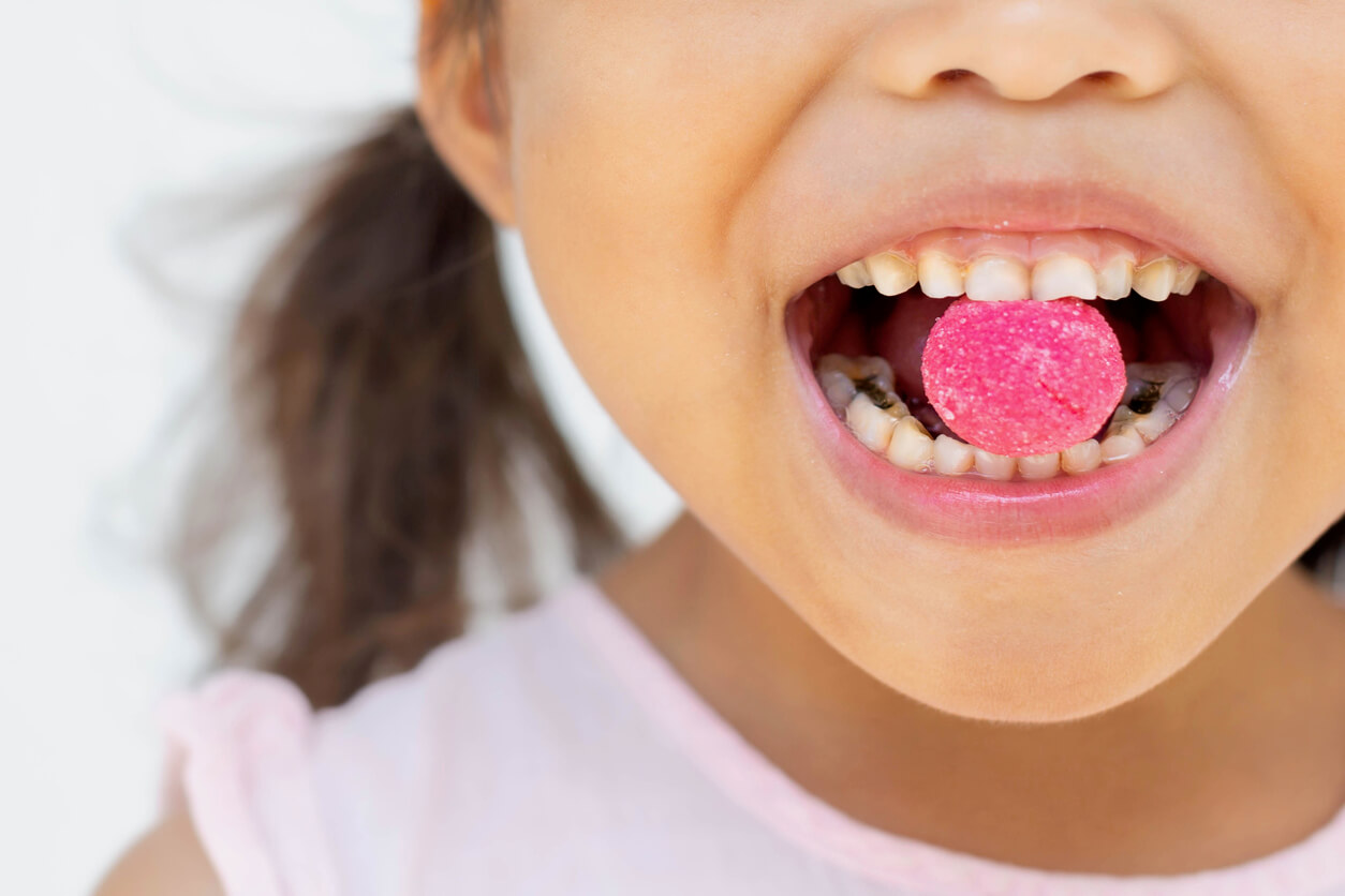 En liten flicka med hål i tänderna som biter i ett gummiaktig godis.