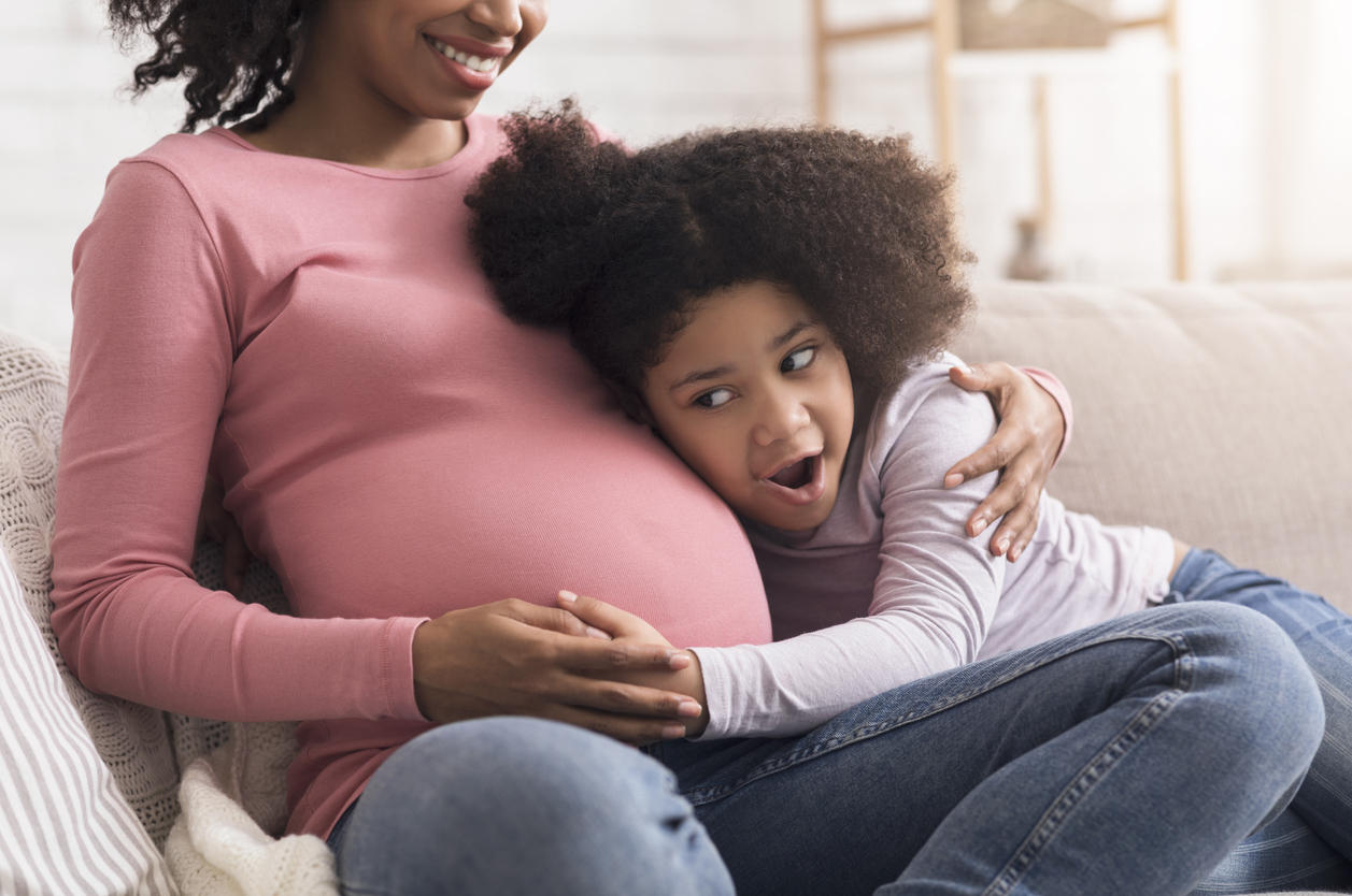 A little girl putting her ear against a pregnant woman's belly.