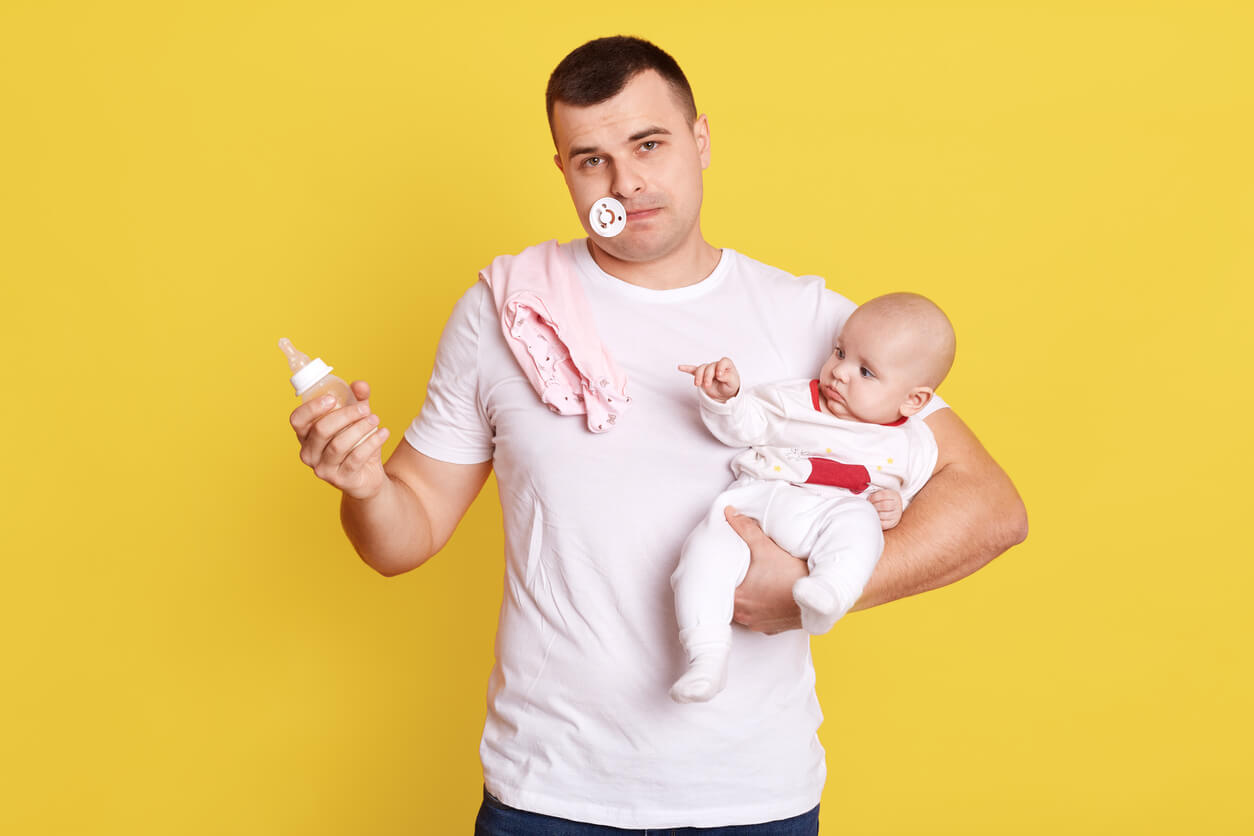 Un père qui tient son bébé dans une main et le biberon dans l'autre.