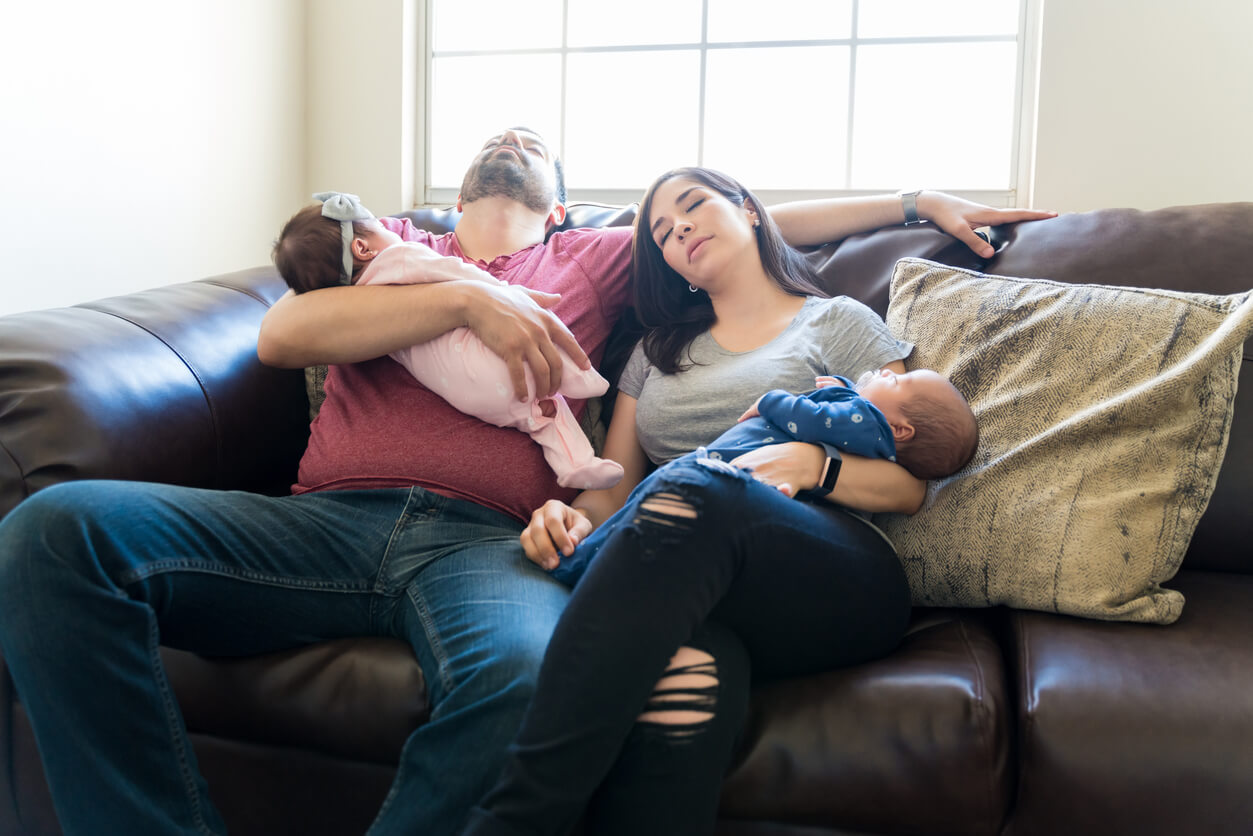 Exhausted parents holding their twin babies while sleeping.
