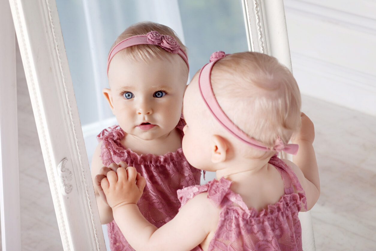 A baby girl looking at a mirror.