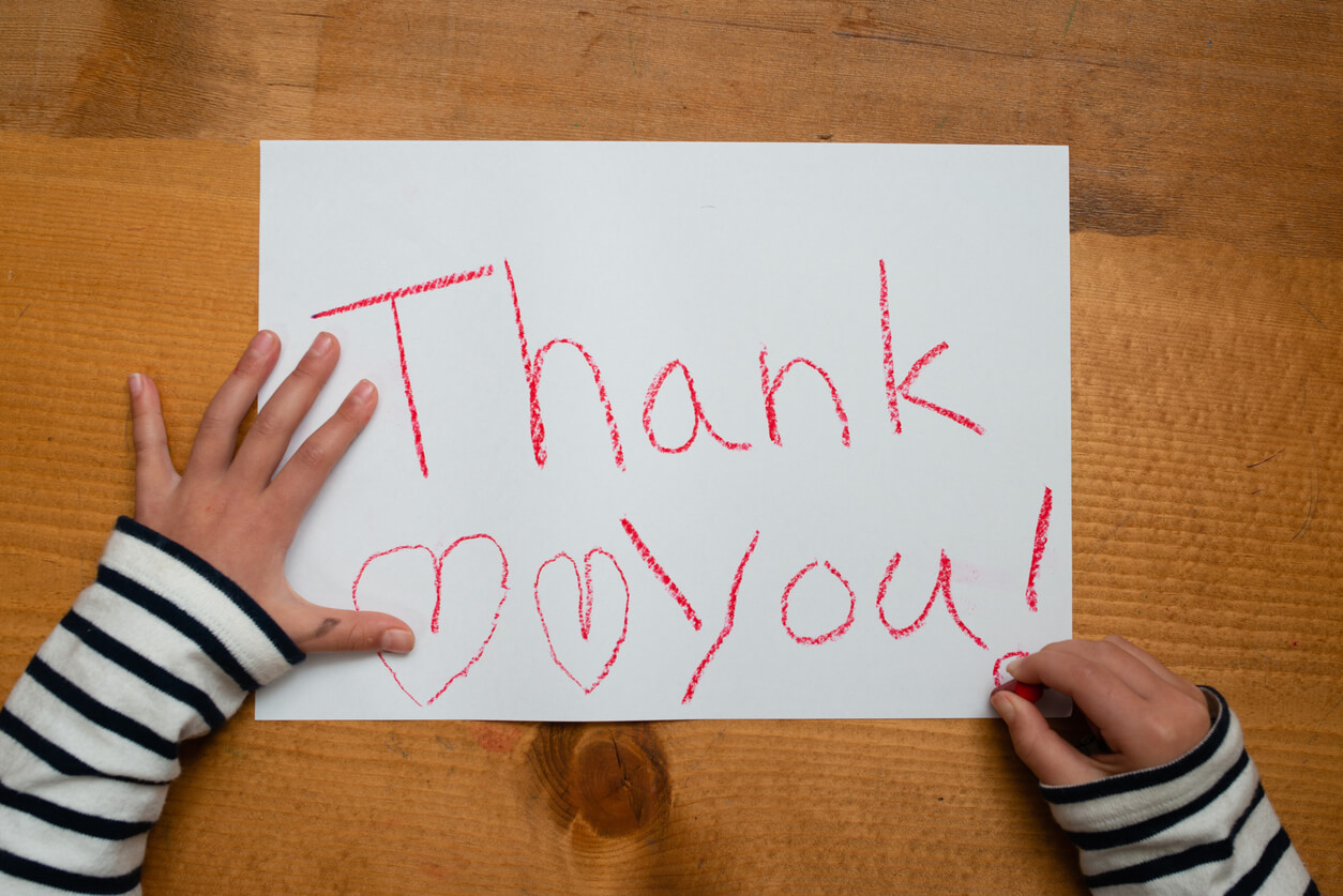 Et barn som skriver "Takk" på et papir med en rød fargestift.