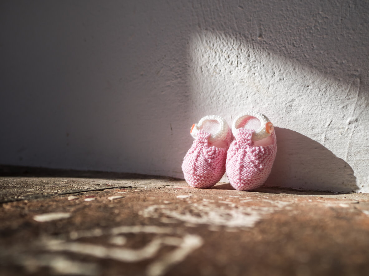 A pair of pink baby booties leaning against a wall.
