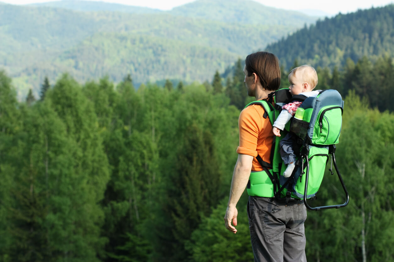 Un père avec son bébé sur le dos à la montagne.