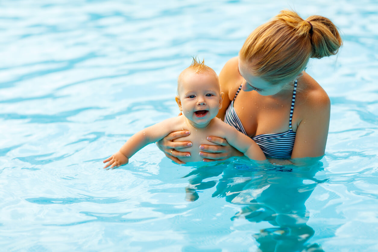 A woman holding her baby in the pool.