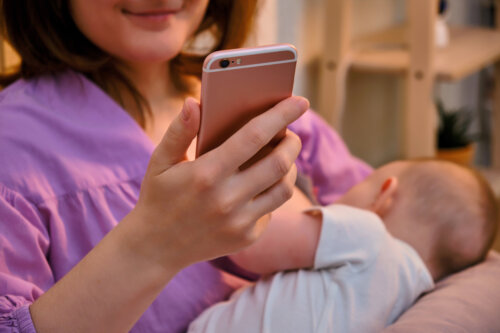 madre con telefono en mano mientras da el pecho a su bebe