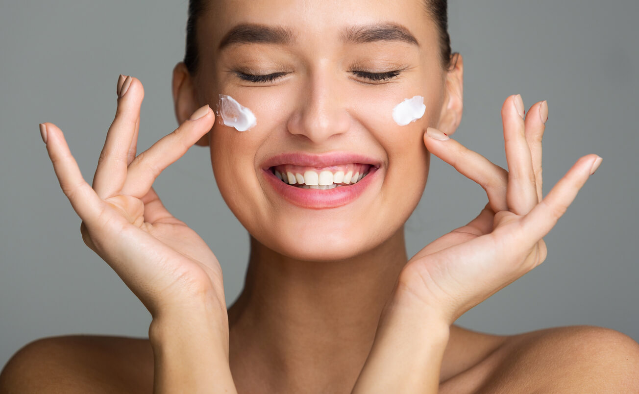 mujer feliz con aplicacion de crema en el rostro