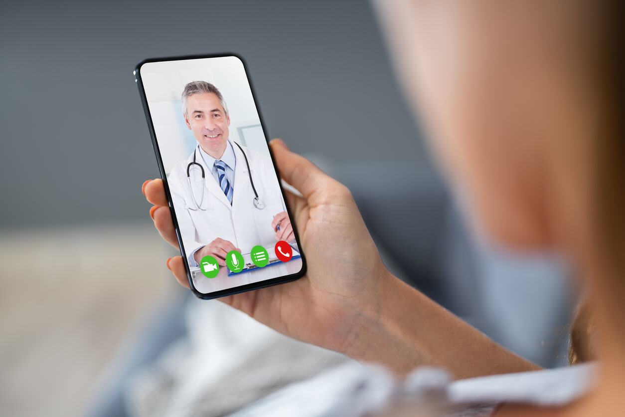 mujer sostiene telefono movil para teleconsulta videollamada con el medico