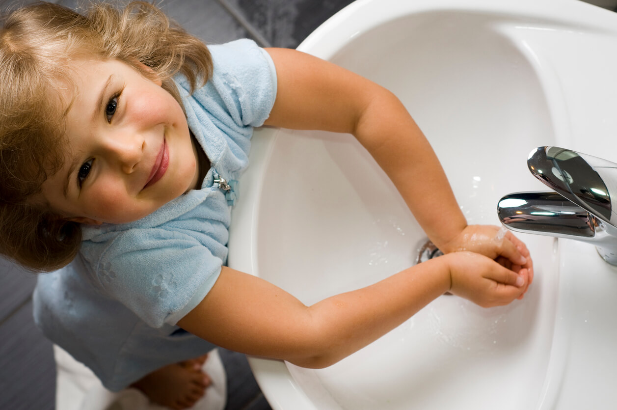 A toddler washing her hands in the sink.