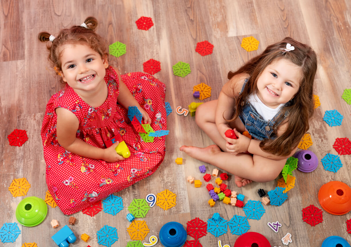 Two small girls playing on the floor and smiling up at the camera.