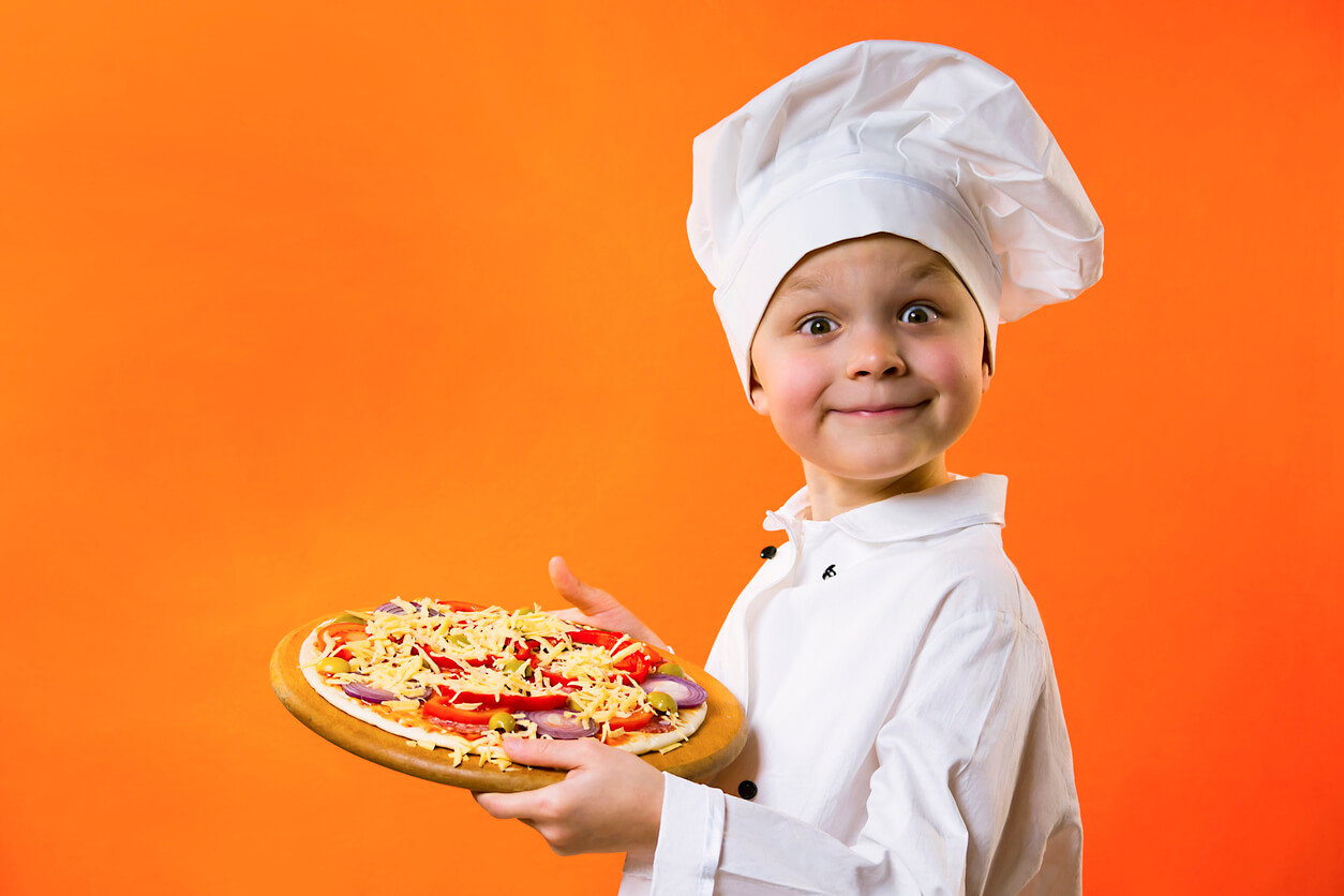 A child dressed as a chef carrying a pizza.