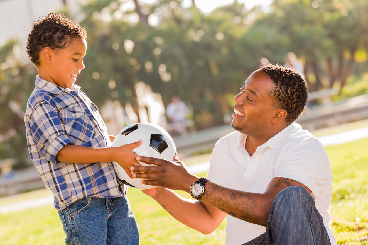 A father handing a soccer ball to his young son.