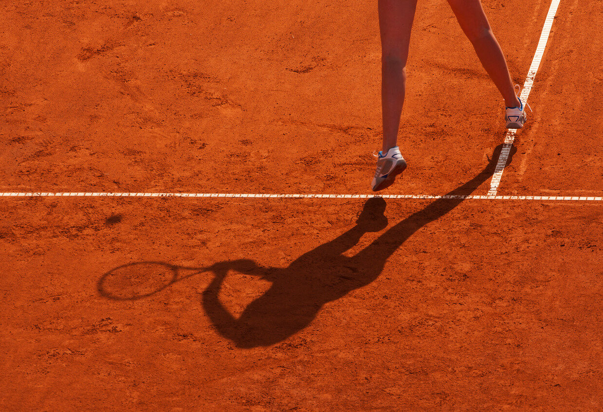 jambes de femme sur un court de tennis en terre battue.
