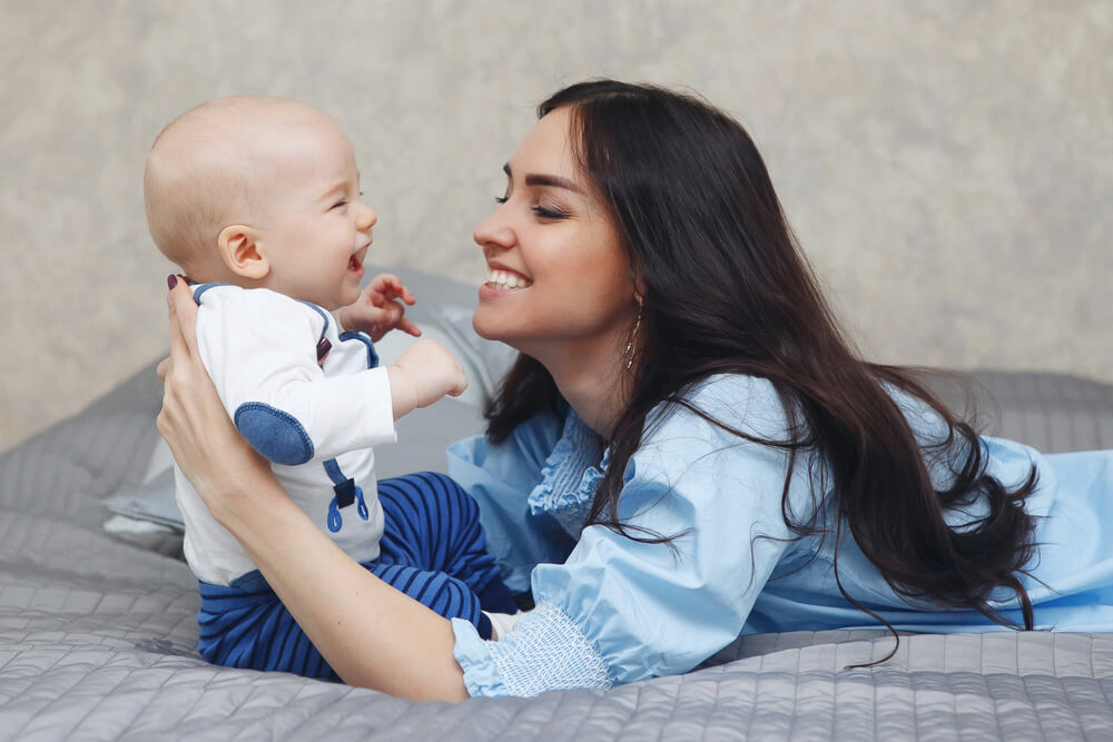 En mamma som ligger i sängen och leker med sin bebis.