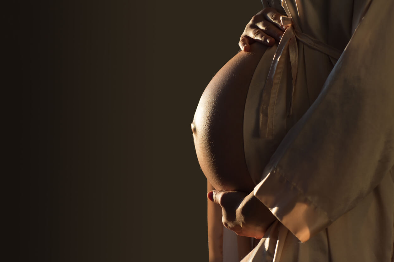 En gravid kvinne iført en satengkåpe og holder magen hennes.