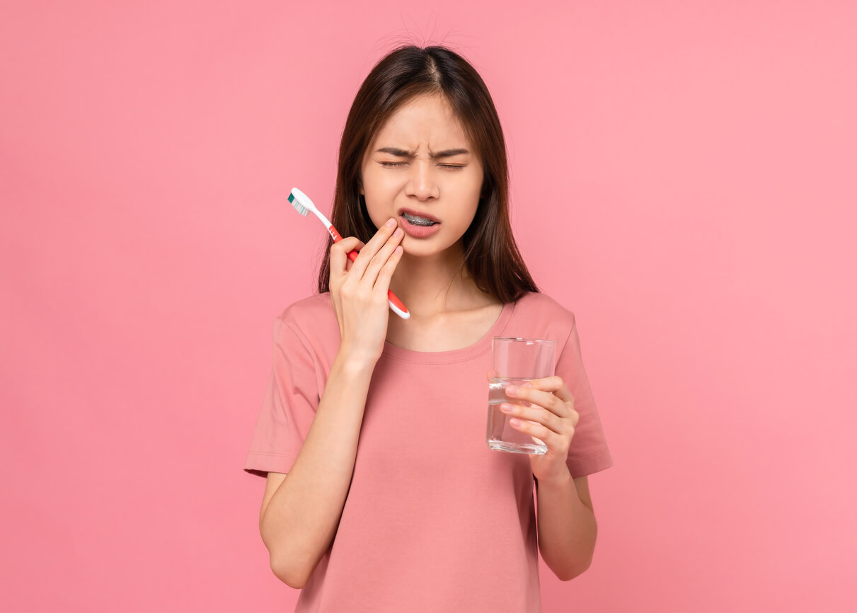 jovem adolescente agarra a boca dor de dente escova de dentes copo de água