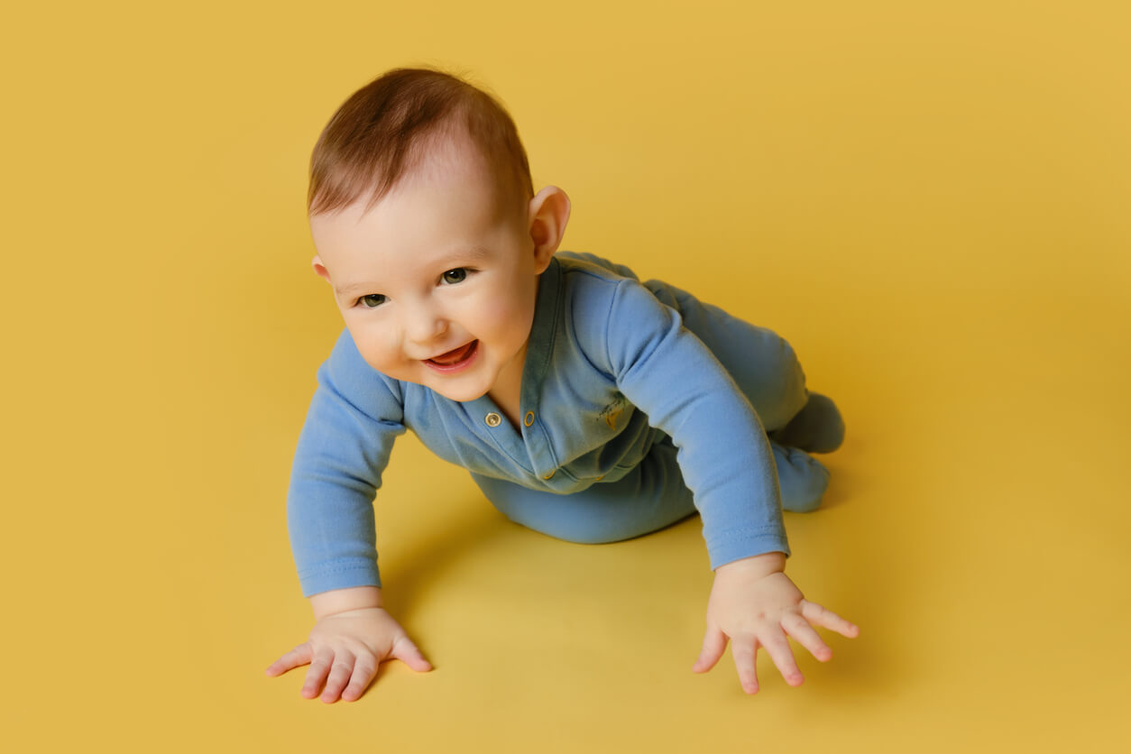 A baby boy crawling and smiling.