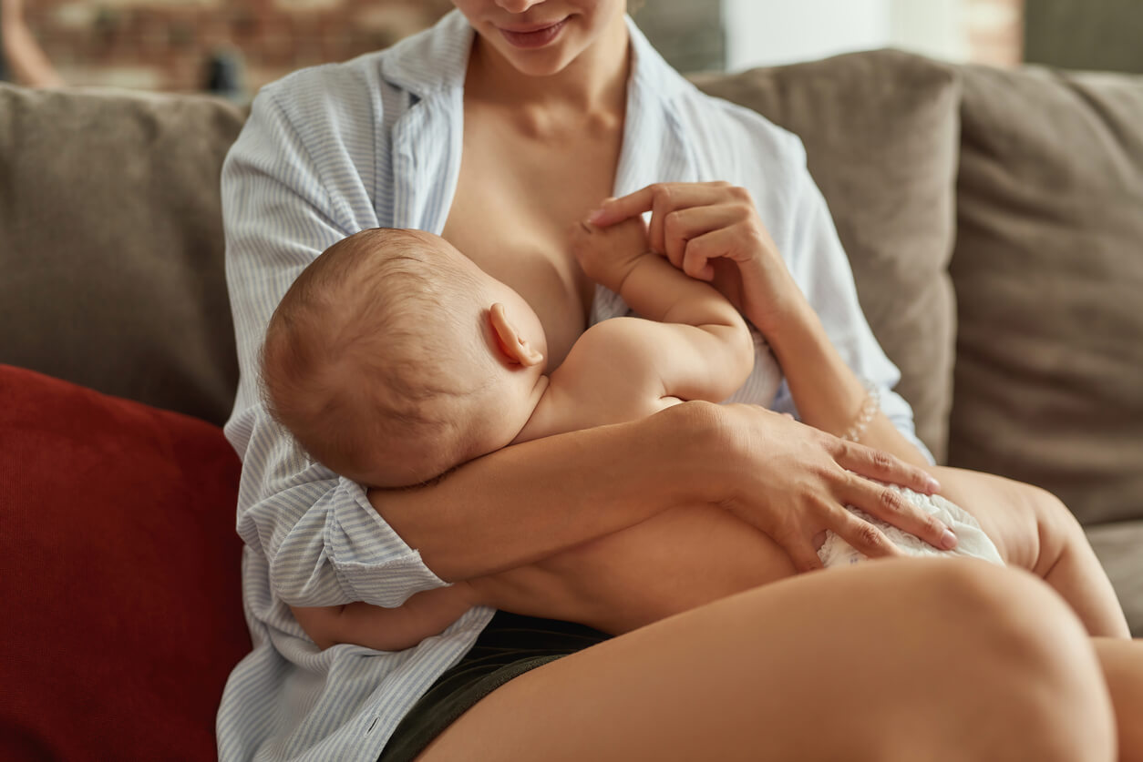 Mujer da el pecho a su bebe sentada en el sofá de la casa cómoda