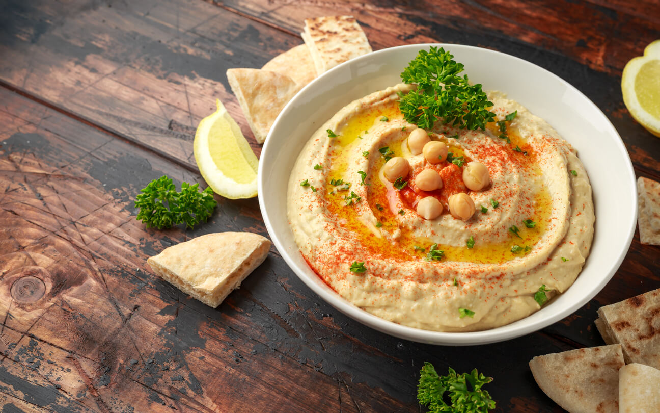 A bowl of hummus surrounded by pieces of pita bread.