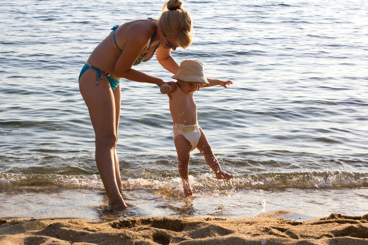 A mother splashing with her toddler on the beach.