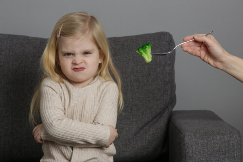 nina cara enojo asco con mano adulto tenedor brocoli