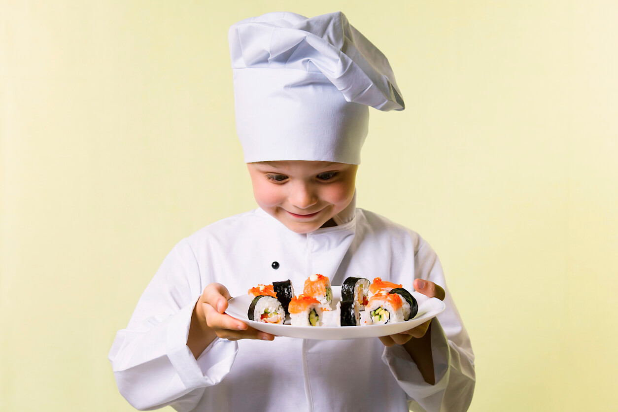 un garçon habillé en cuisinier tient une assiette avec des morceaux de sushi
