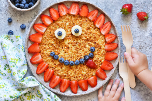 manos de bebe agarran tenedor panqueque de avena con frutilla arandanos banana