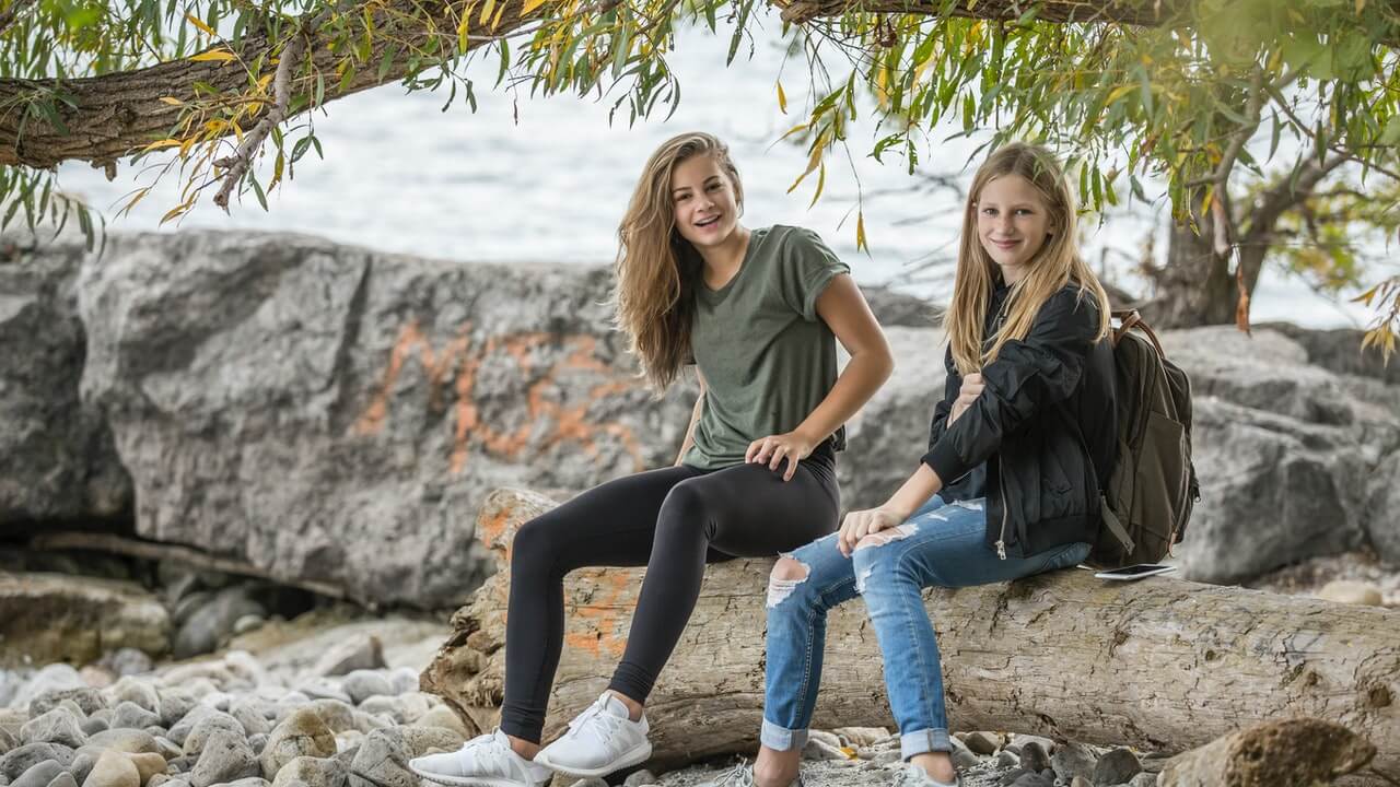 To tenåringsjenter sitter på en tømmerstokk ved sjøen.