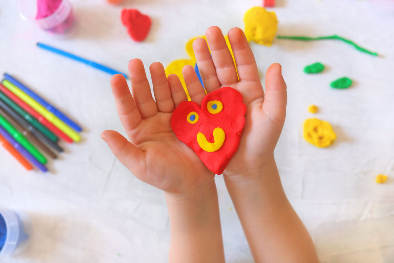 A child holding a heart with a smily face made of play dough.