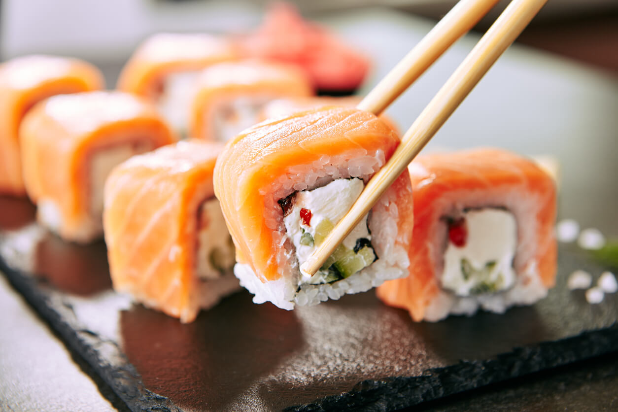 paito chino sostiene pieza de sushi rollo roll salmon arroz queso verdura