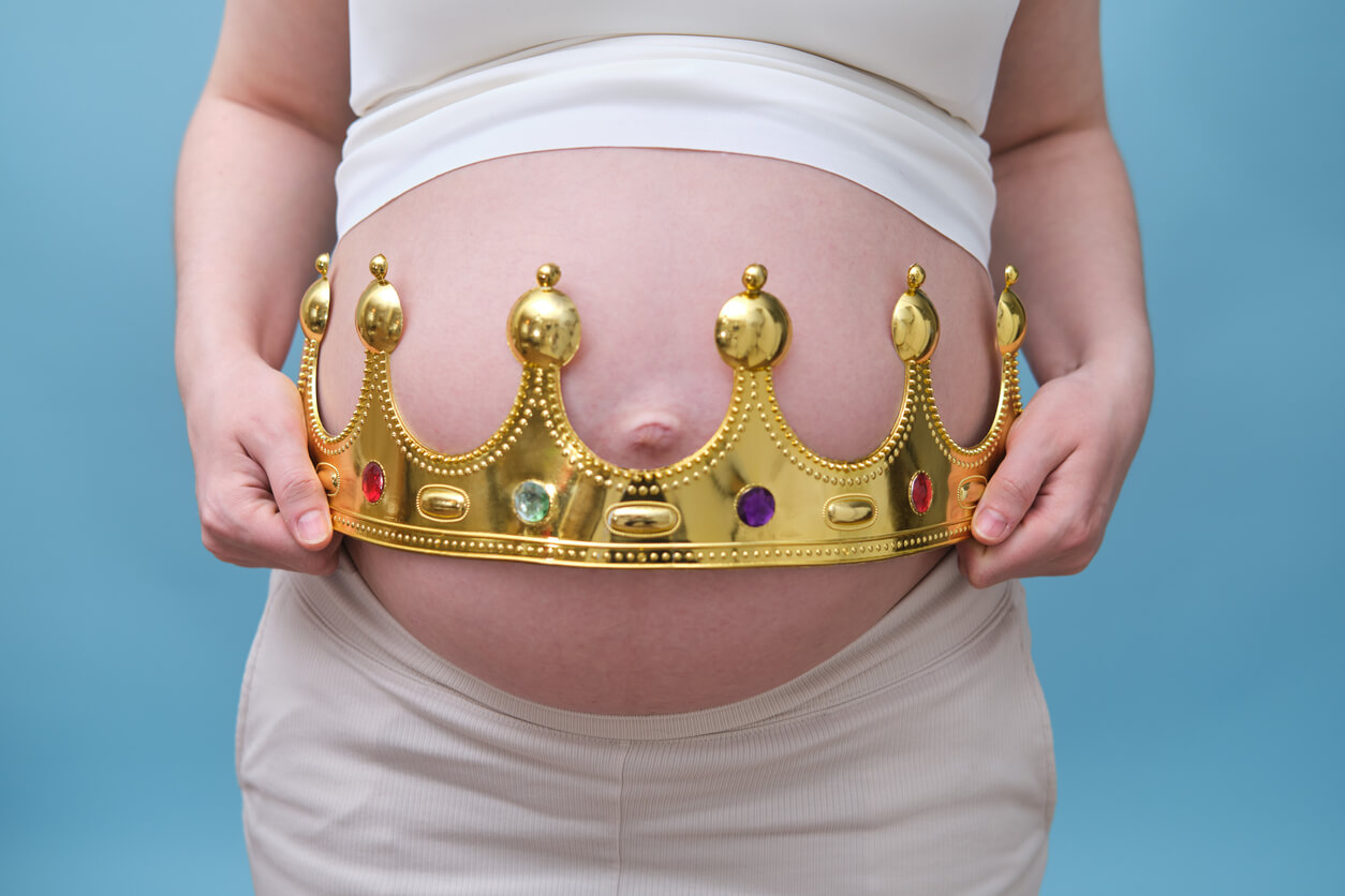 A pregnant woman holding a crown over her belly.