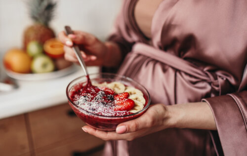 embarazada en bata con plato de frutas y cereales en la mano