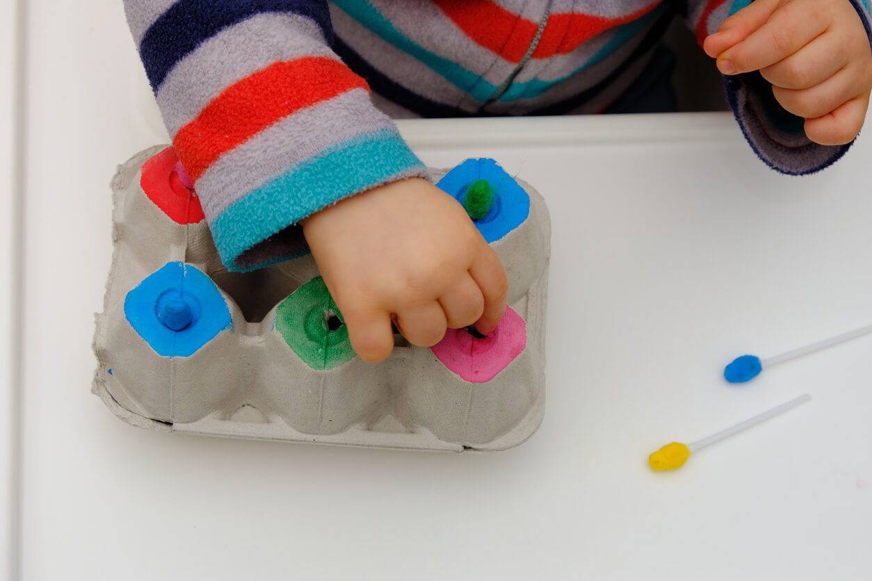 A toddler playing a game with an egg carton.