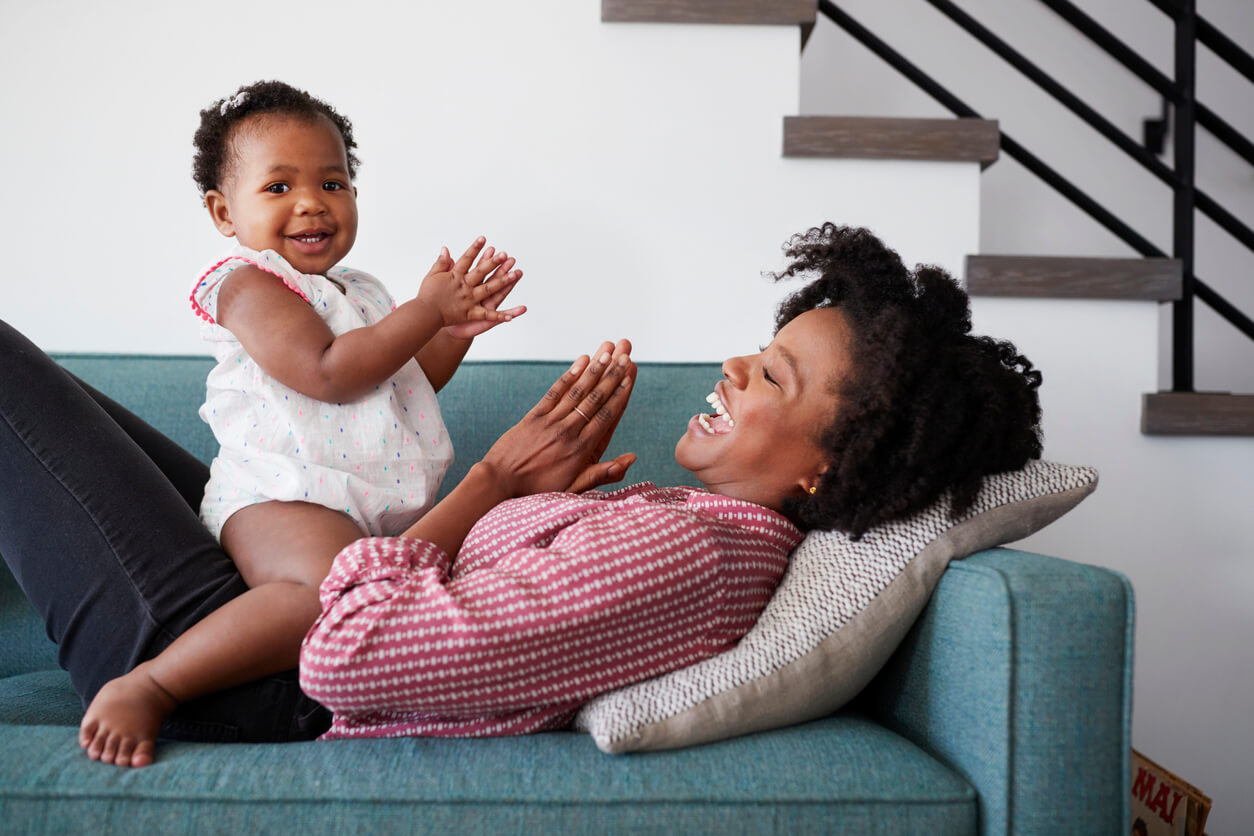 A mother and her toddler daughter clapping and laughing.