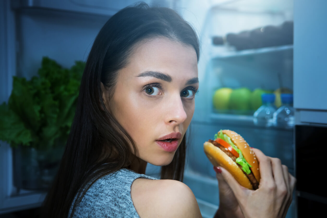 joven mujer come hamburguesa a a escondidas en la madrugada noche hambre emocional atracon culpa ansiedad