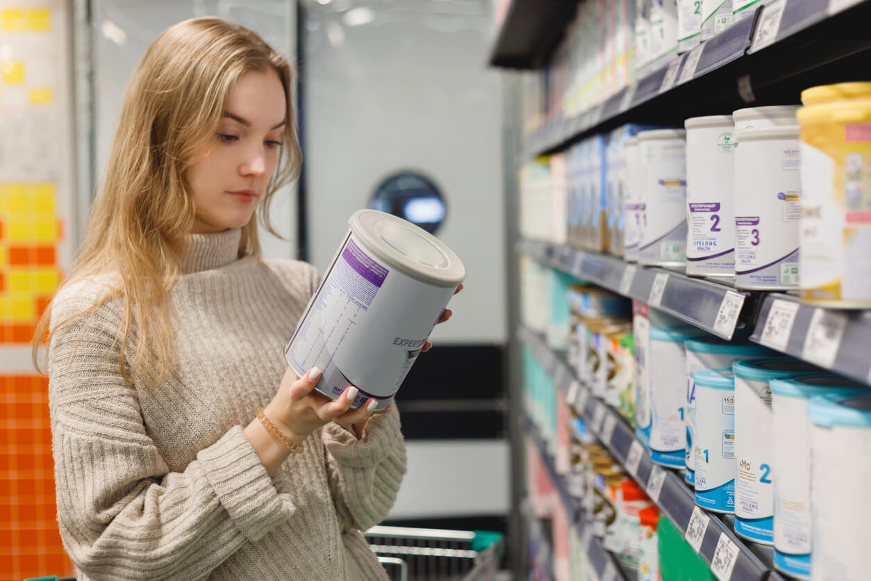 mujer madre en la gondola de la farmacia supermercado lee etiquetado del producto leche de formula inicio continuacion