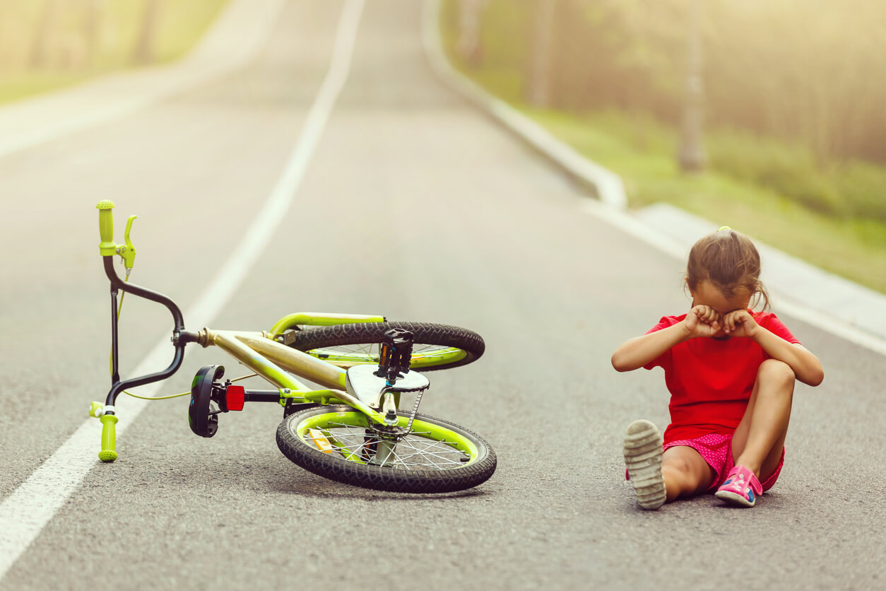 En liten flicka som gråter för att hon har ramlat av sin cykel.