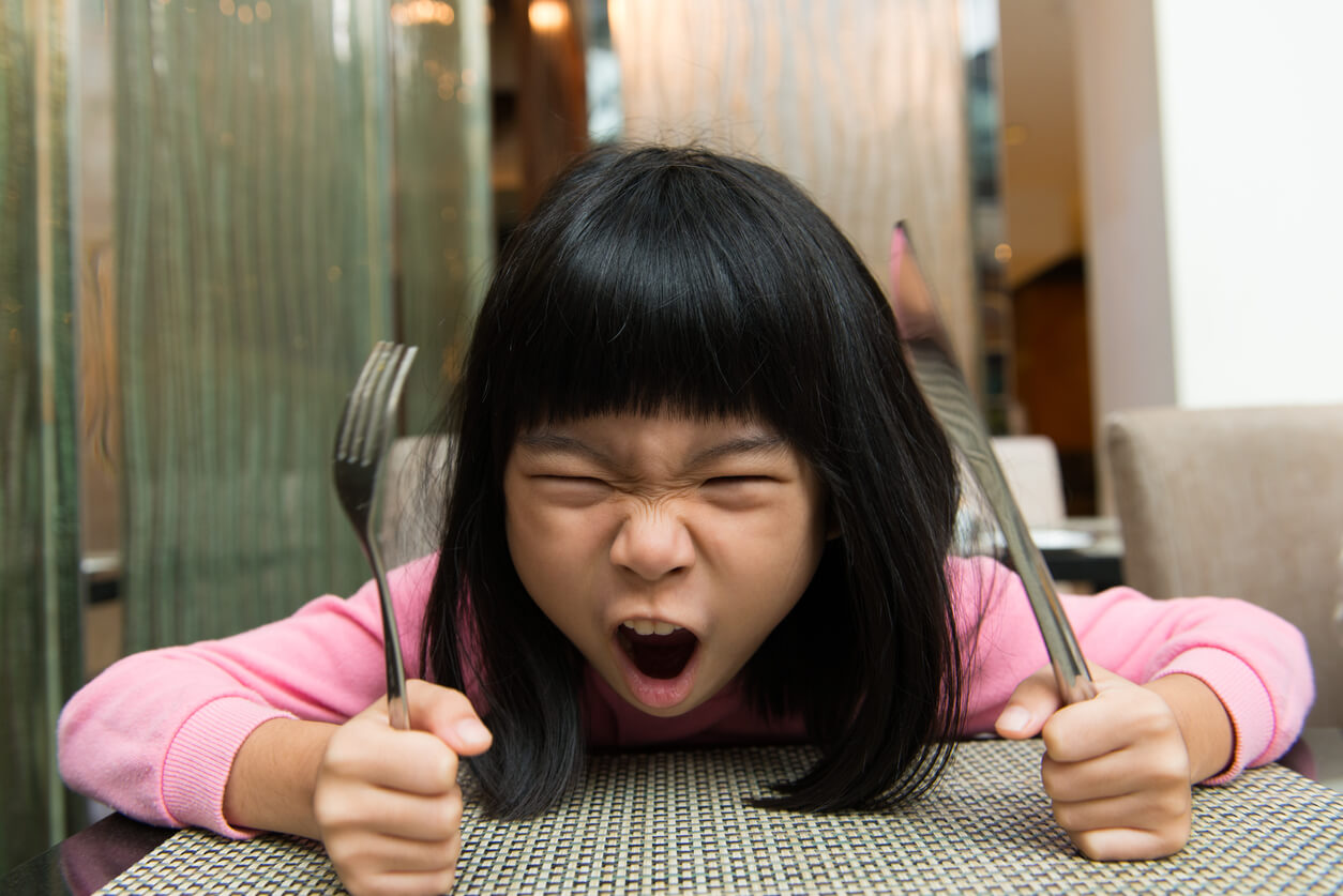 Petite fille au visage en colère affamé, impatient, couteau, fourchette, couverts, table