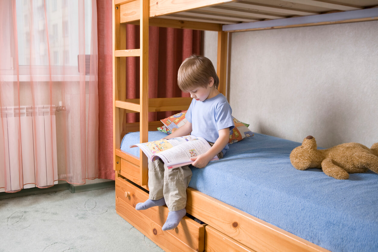 A child sitting on a lower bunk reading a book.