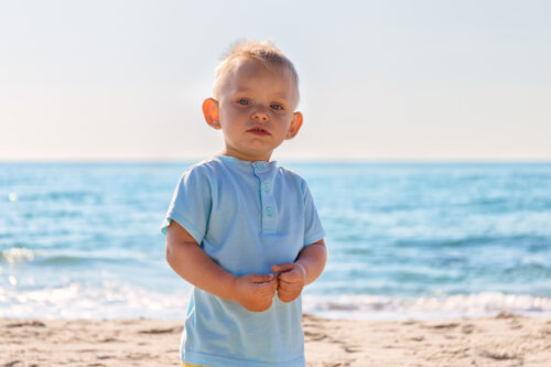 niño orejas grandes salidad de soplillo mira a la camara en dia de sol en la playa arena mar