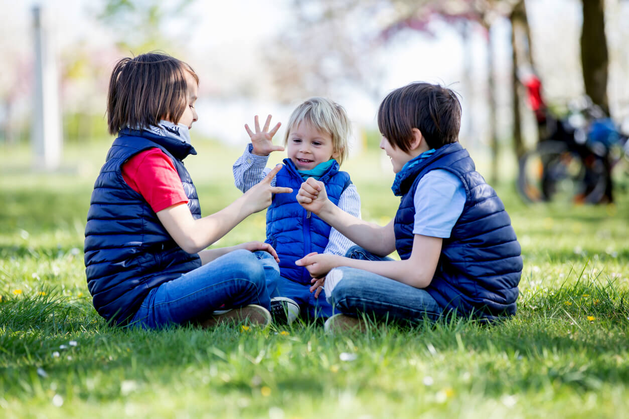 Three young boys playing rock paper scissors while sitting in the grass.